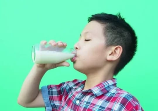 A boy drinking milk in a glass bottle.