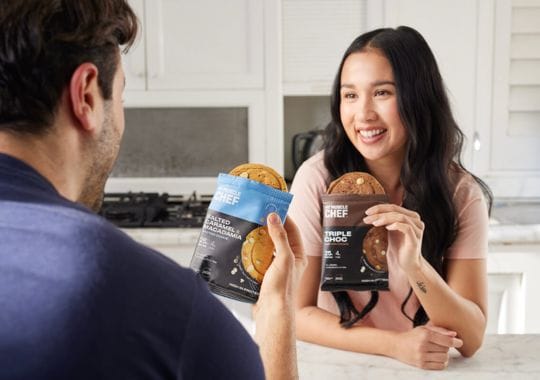 A man and a woman holding protein cookies.