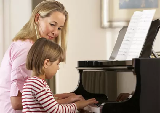 A woman teaching the little girl how to play a piano.
