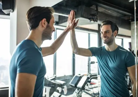 Reflection in a mirror of a happy man giving himself high-five in a gym.