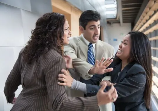 2 young executives fighting while a co-worker tries to separate them.
