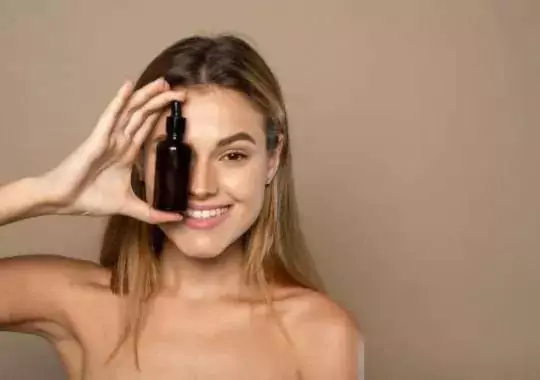 Smiling Woman Holding Vitamin C Serum near Her Face.